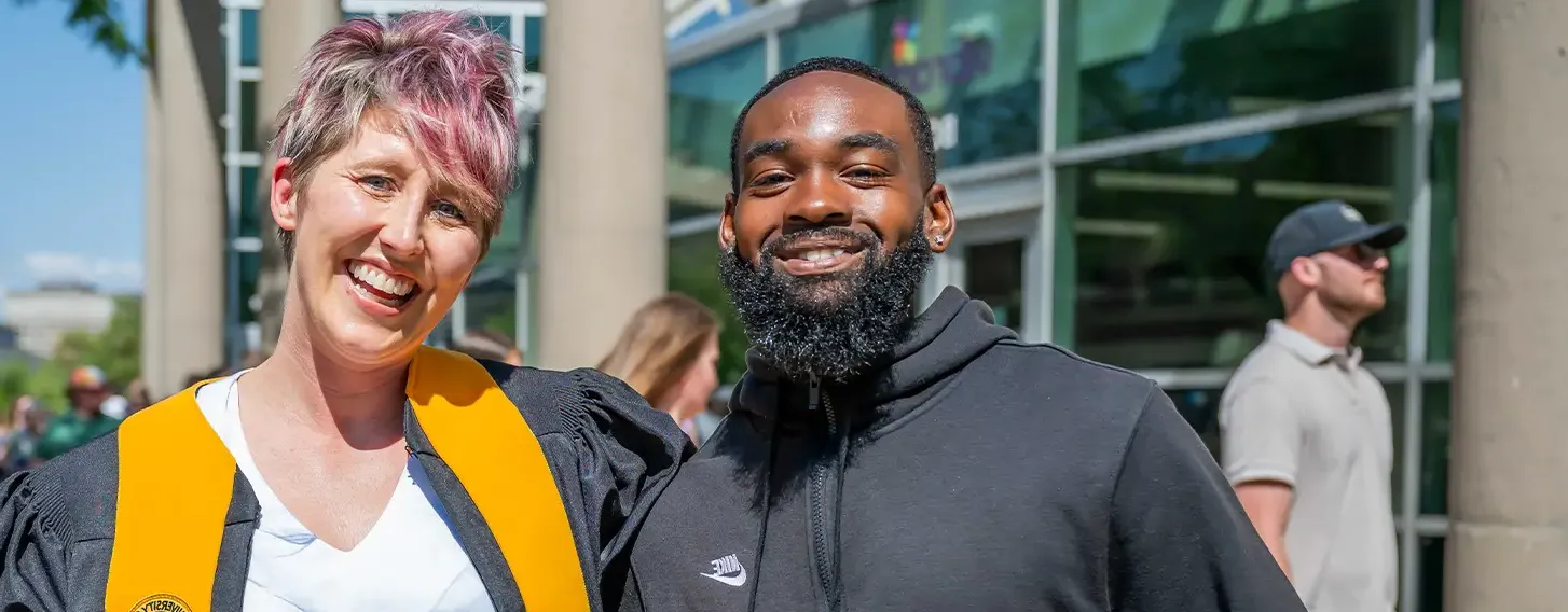 A 教师 member and a student posing together outside at commencement